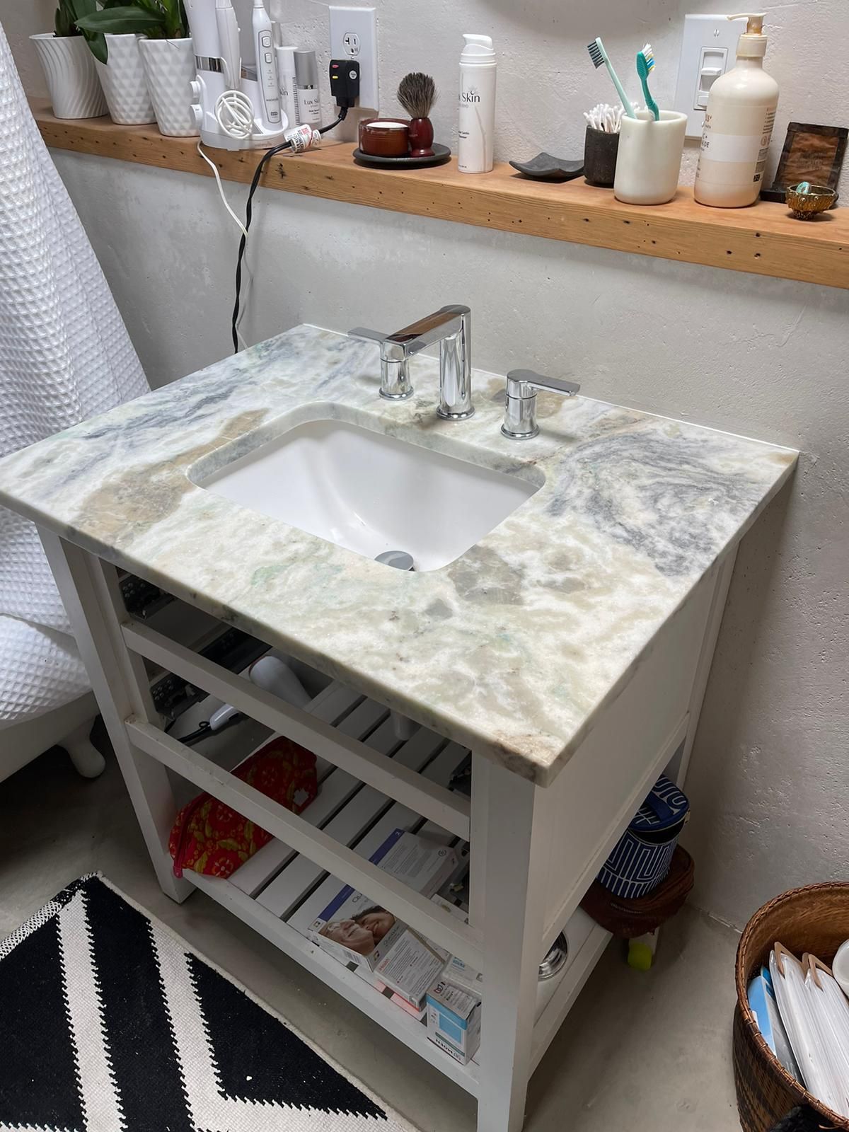 A bathroom sink with a marble counter top and a shelf underneath it.