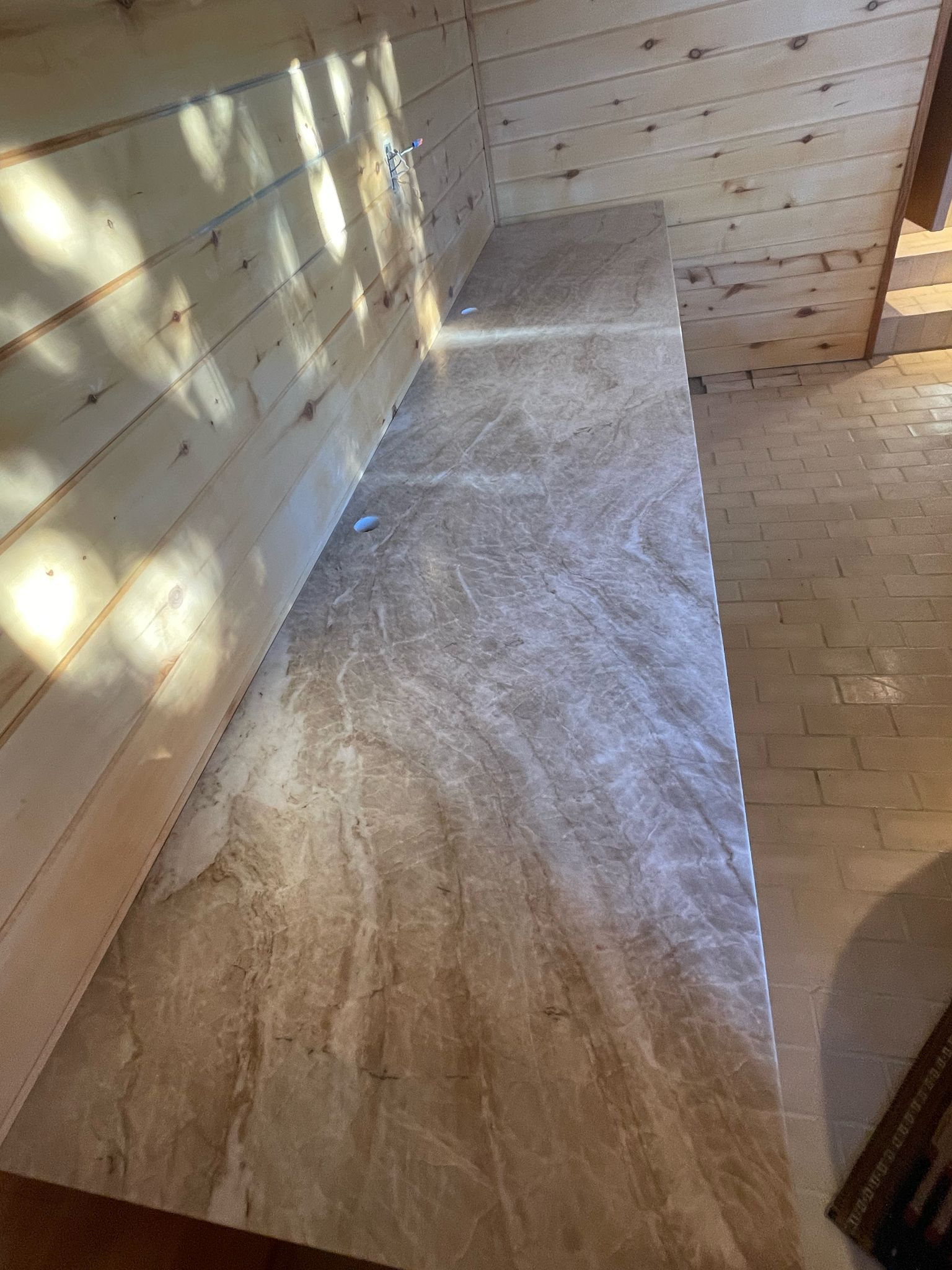 Wooden paneling and a long, light-brown marble-like surface. Light shines from above.