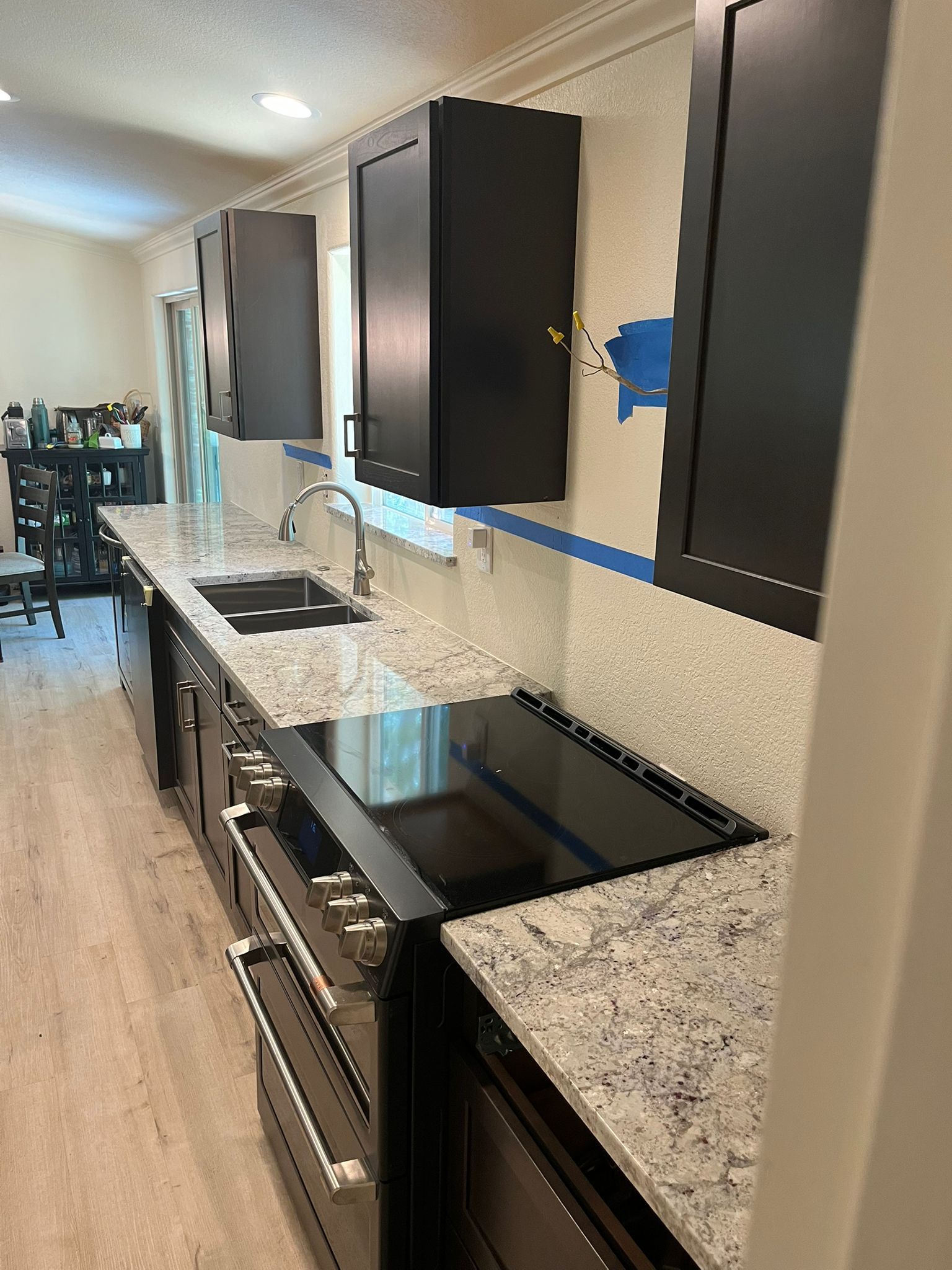 Black cabinets and countertops in a kitchen.  Black cooktop and sink.  Gray and white backsplash.