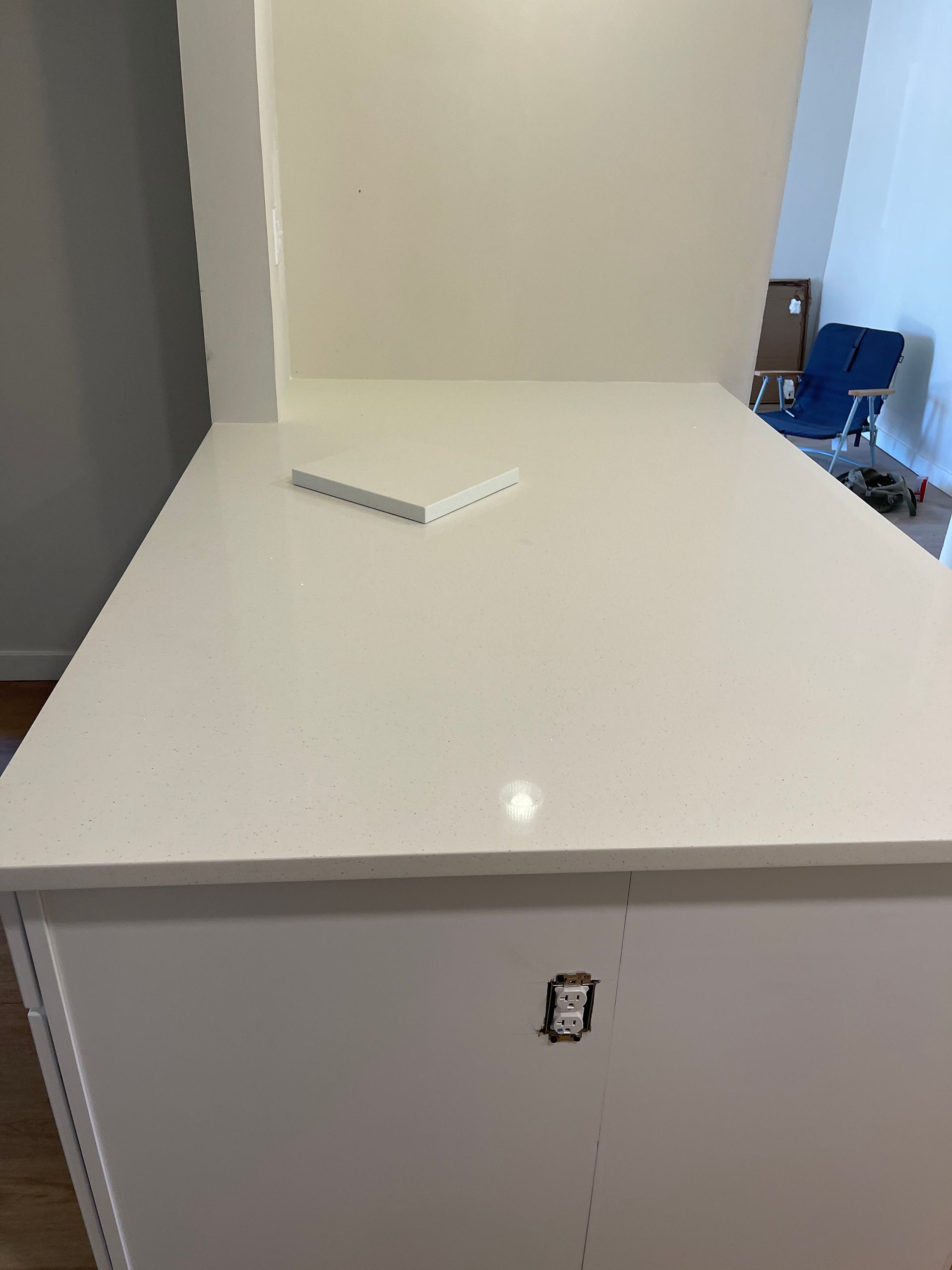 White kitchen island with quartz countertop, partially complete, next to a white wall.