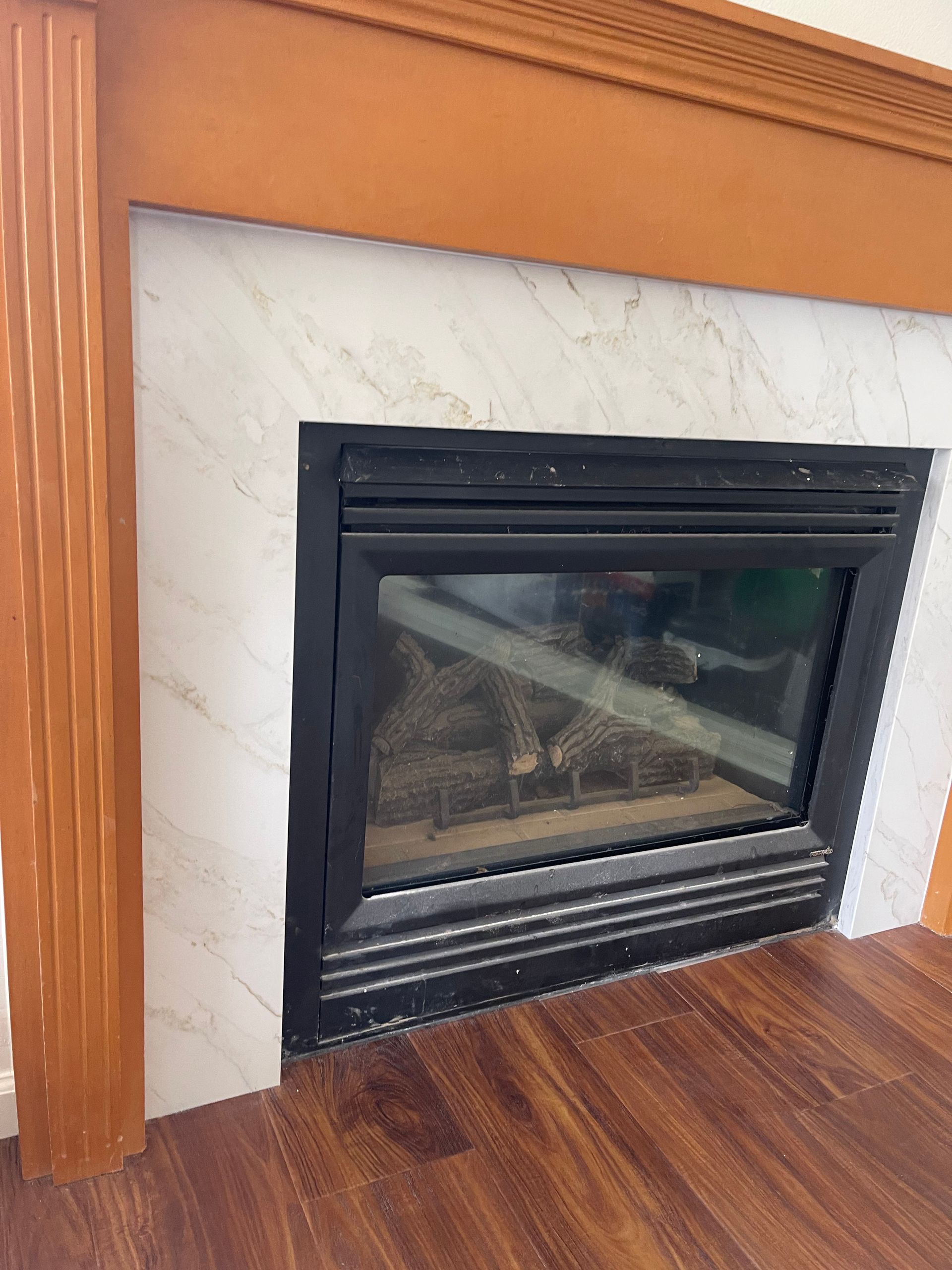Fireplace with black frame, light-colored stone surround, wood mantel and flooring.