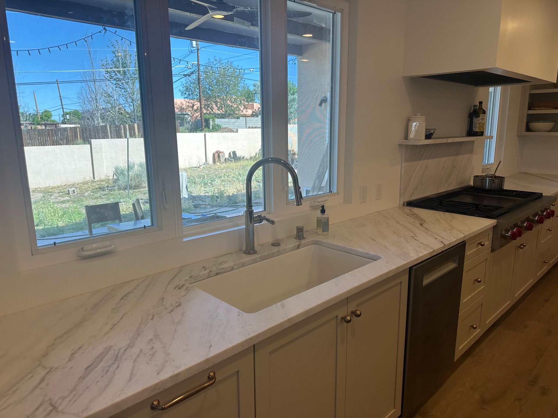 Modern kitchen with white cabinets, marble countertops, and a stainless steel sink and faucet.