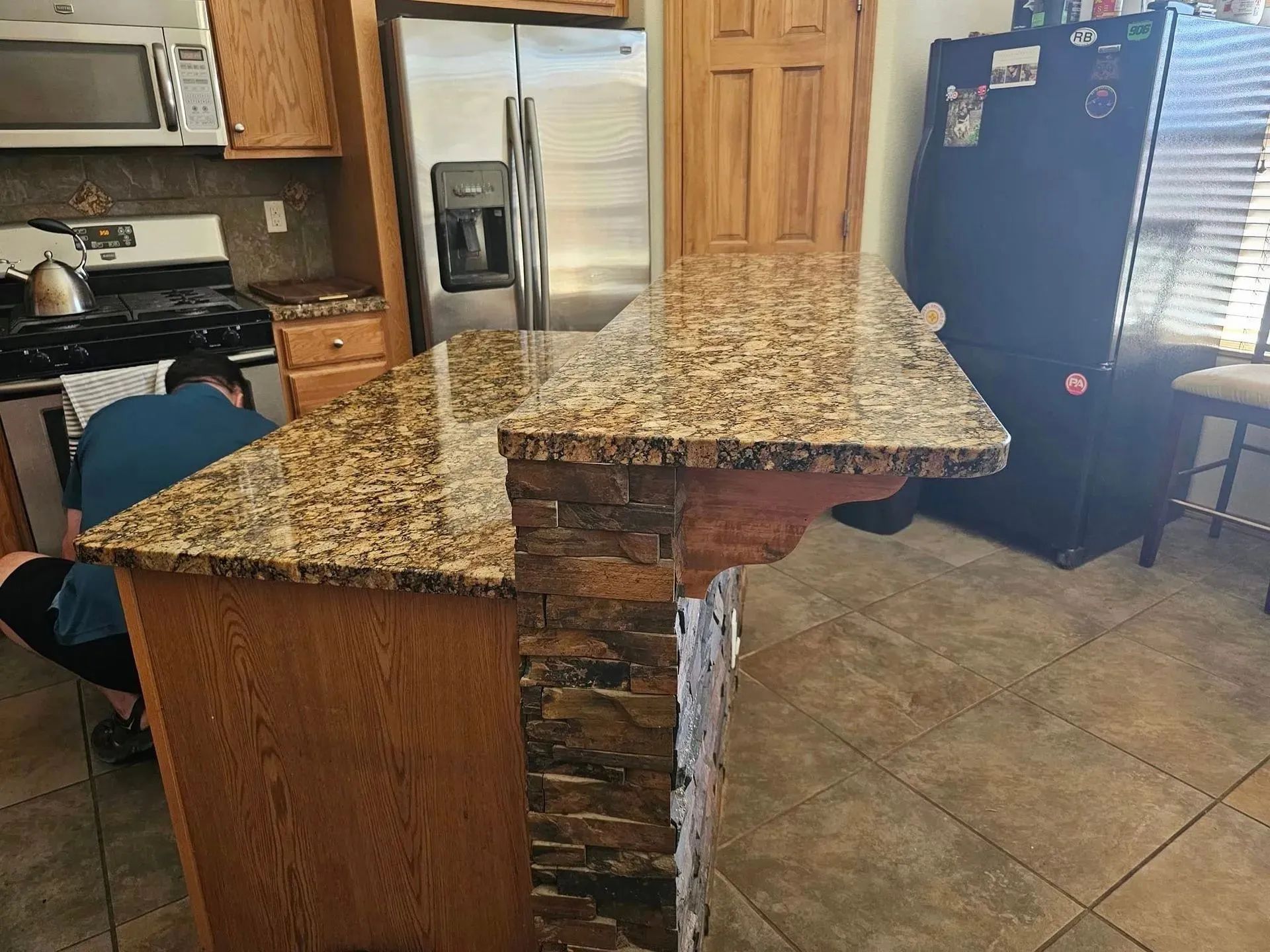 A person works at a kitchen island with a granite countertop and faux brick accents.