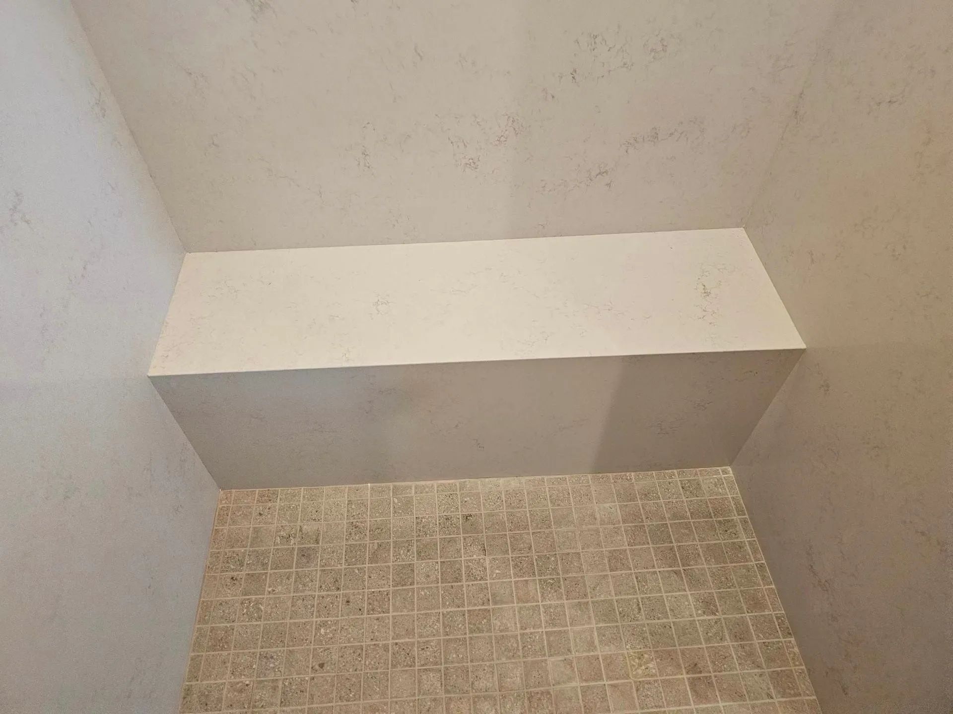 There is a bench in the shower with a tiled floor.