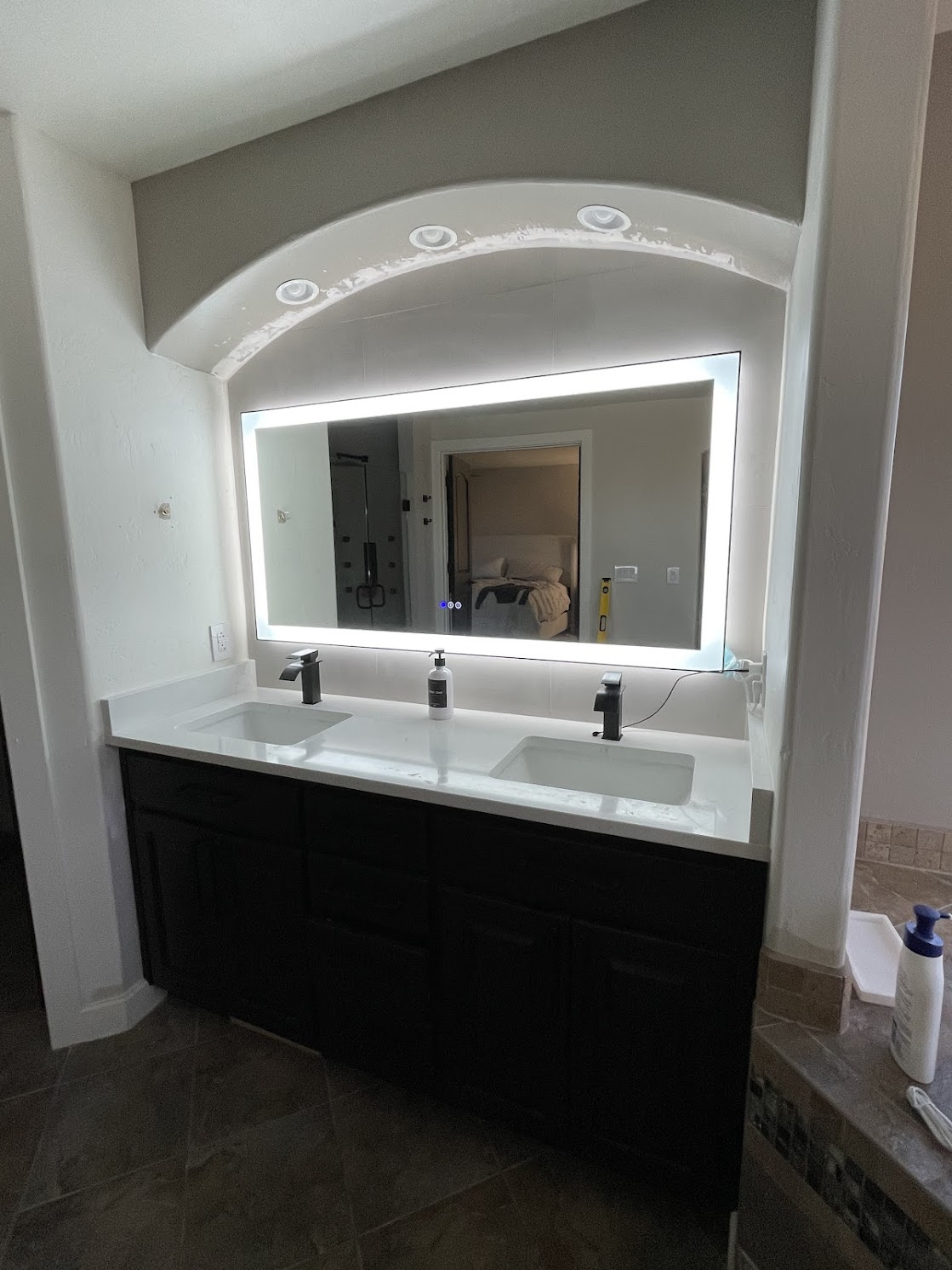 Dark brown double sink vanity with white countertop and backlit mirror in a bathroom.