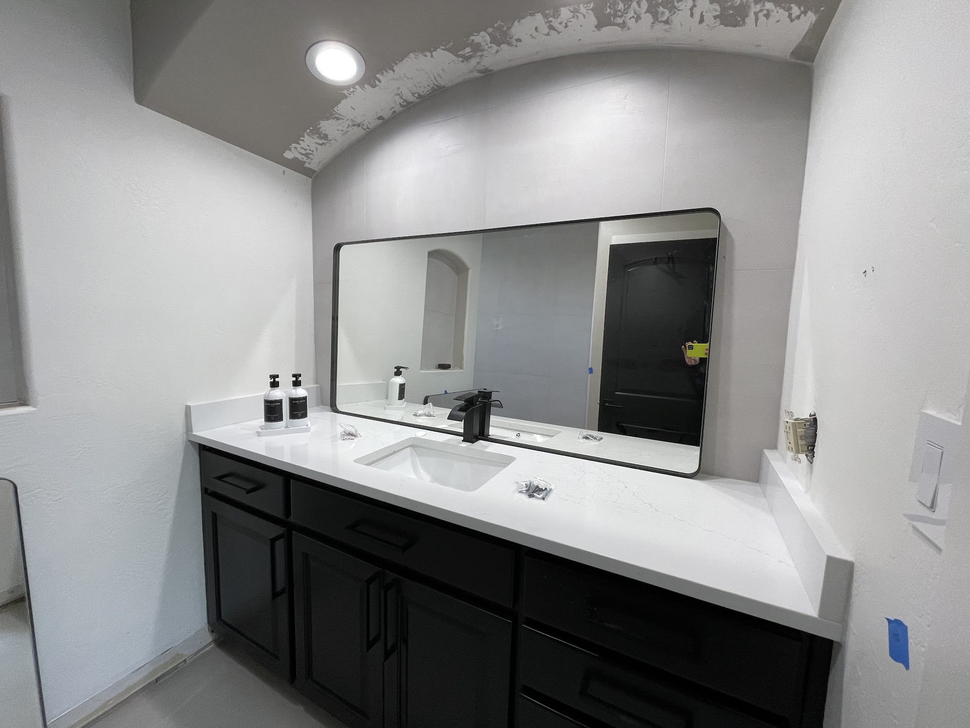 Bathroom with black vanity, white countertop, large mirror, and dark door.