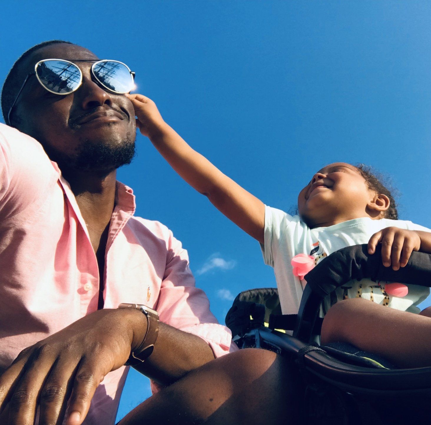 A man wearing sunglasses sits next to a little girl in a stroller