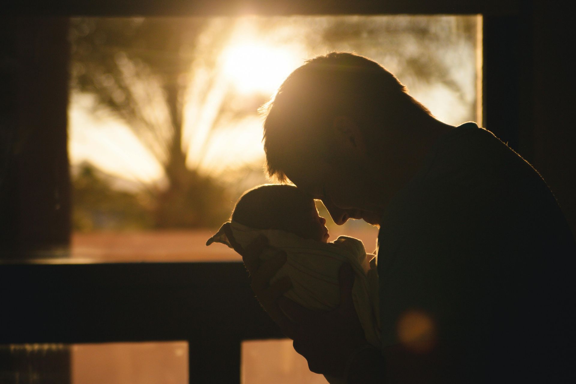A man is holding a baby in his arms in front of a window.