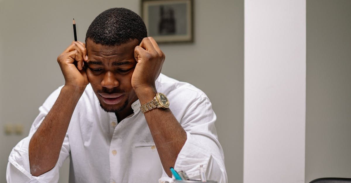 A man is sitting at a desk with his hands on his head.