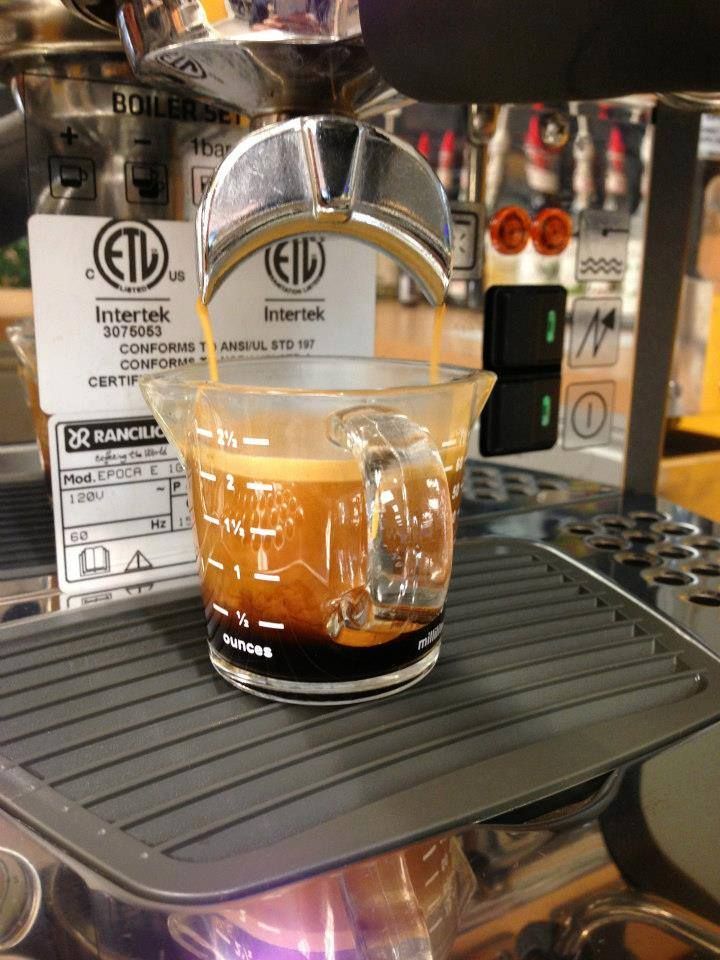 A cup of coffee is being poured into a measuring cup