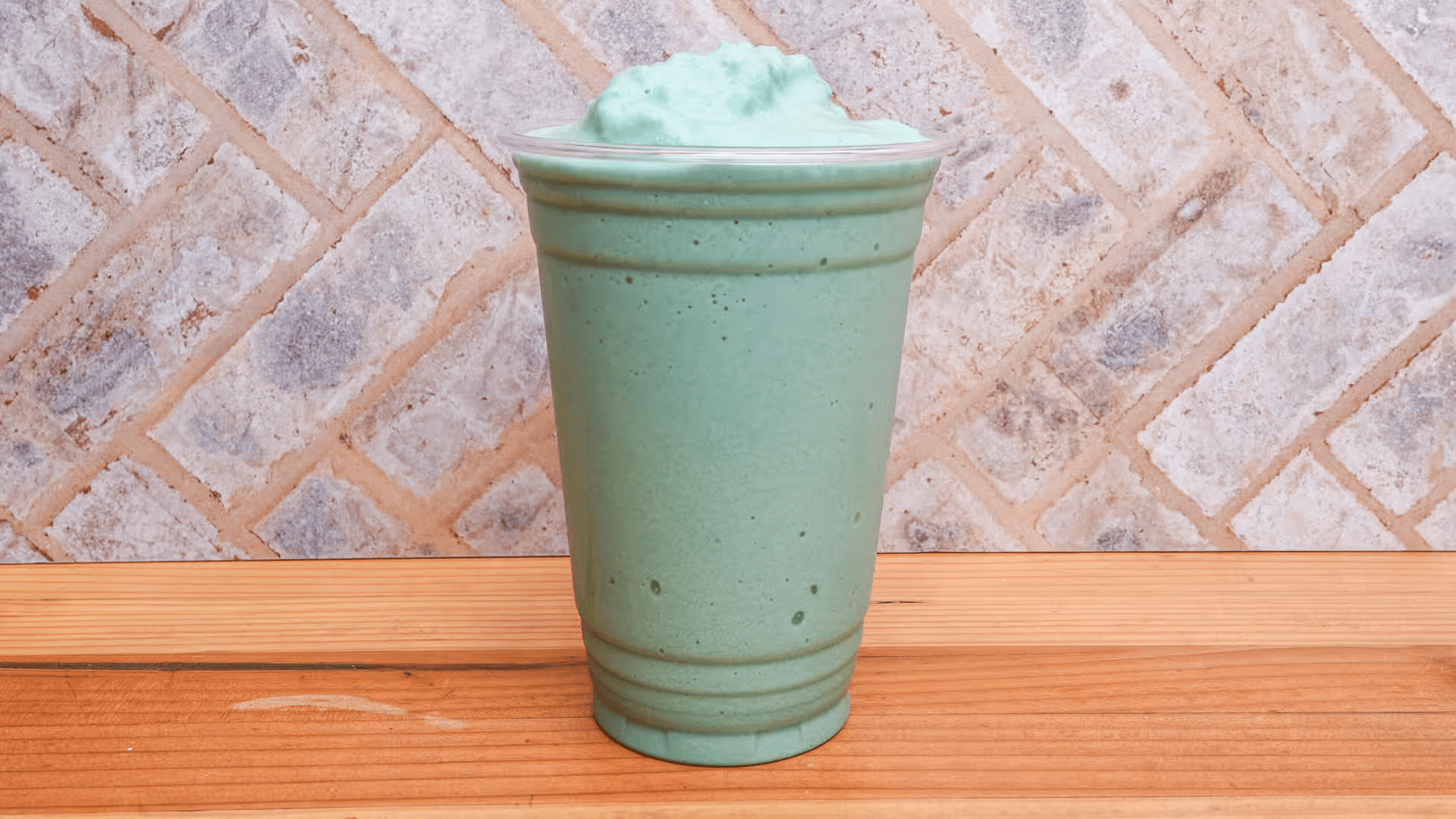 A green milkshake is sitting on a wooden table.