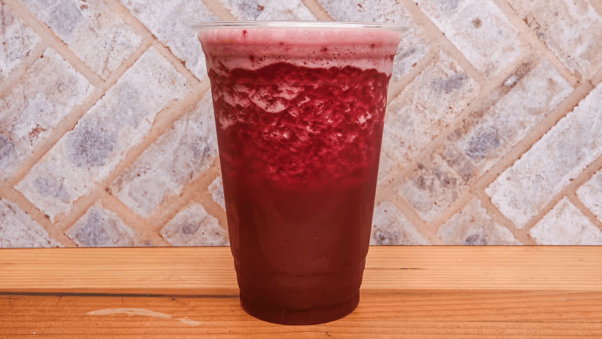 A cup of red liquid is sitting on a wooden table.