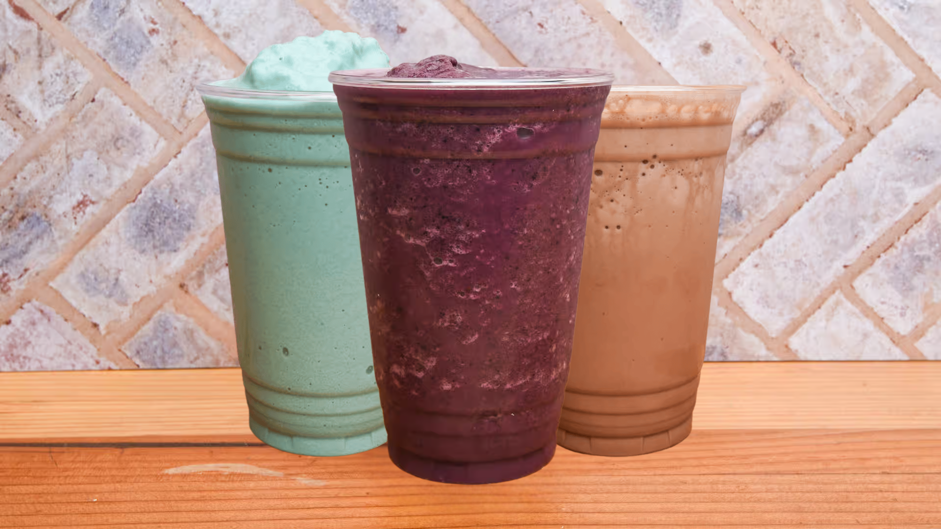 Three smoothies are sitting on a wooden table.