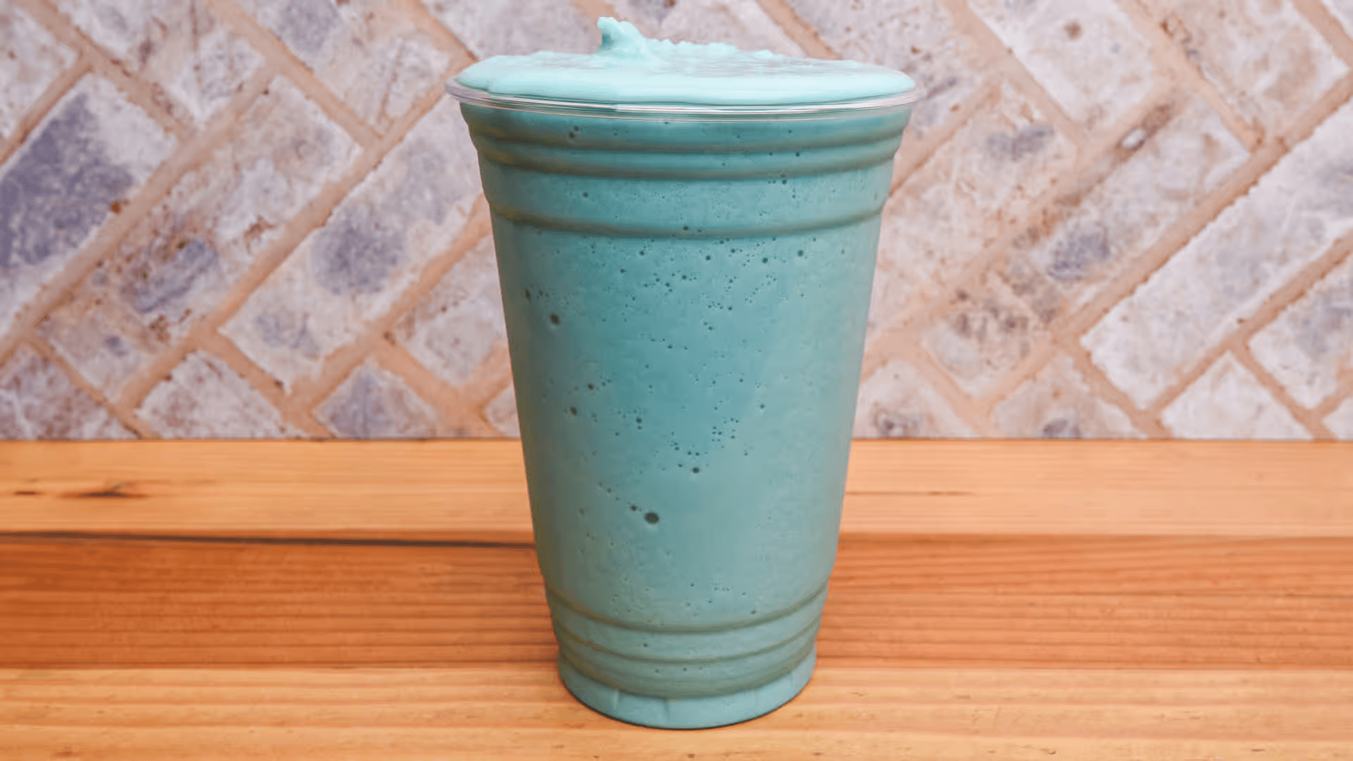 A blue smoothie in a plastic cup is sitting on a wooden table.