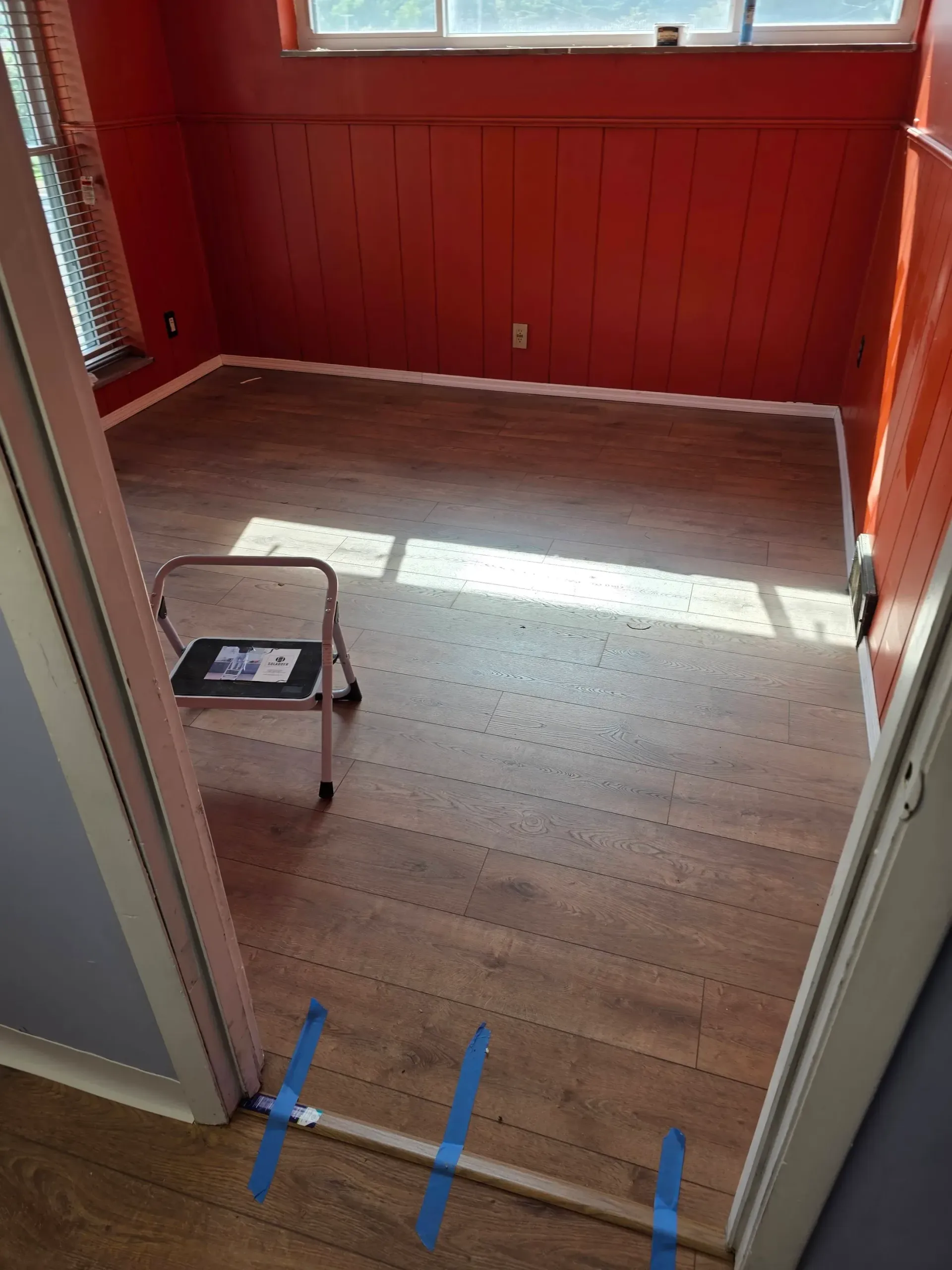 Room with orange walls, wood-look flooring, and a small step stool. Doorway in the foreground.