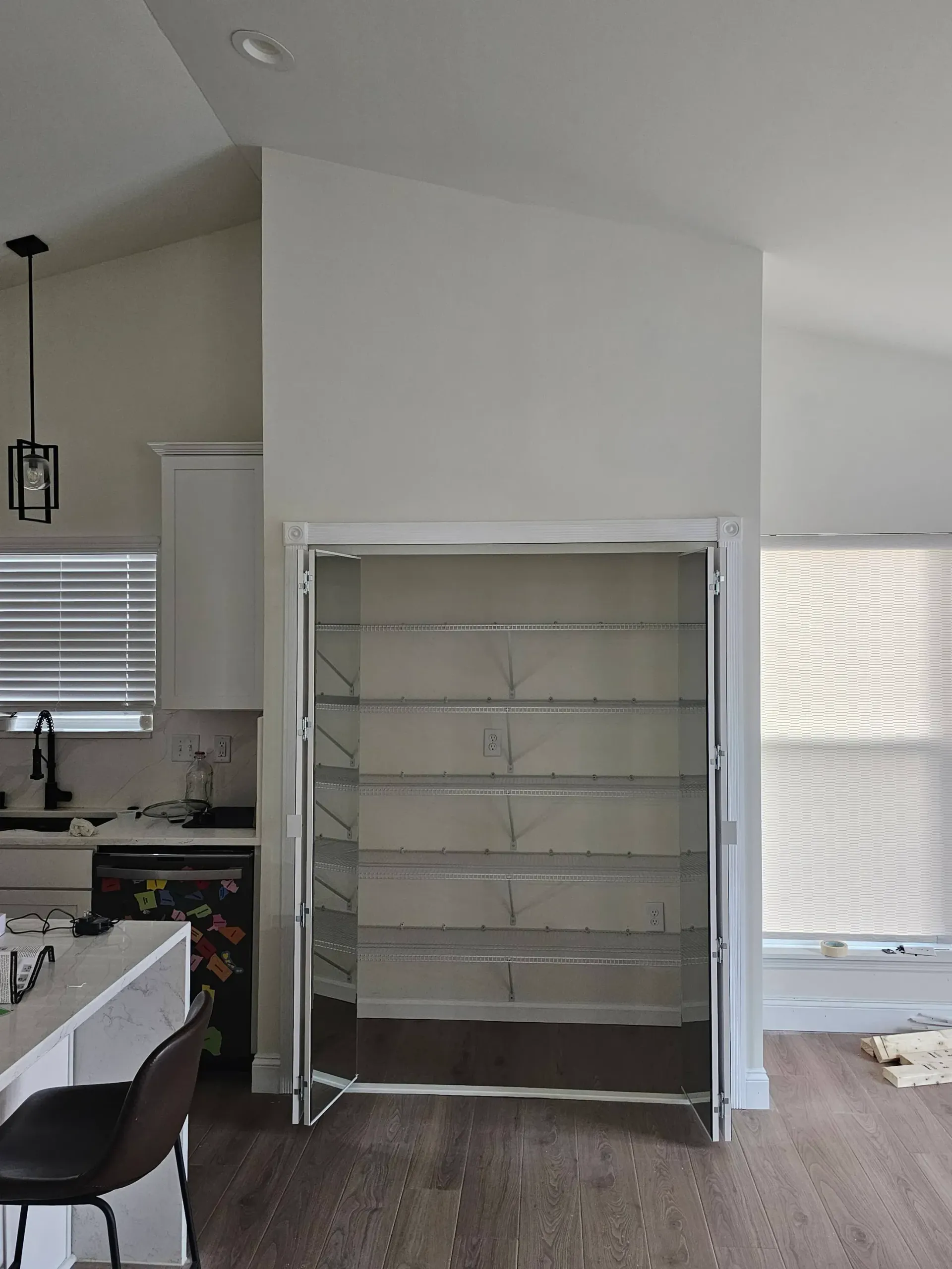Open-shelved closet with metal frames, set in a white-walled room with a kitchen view.