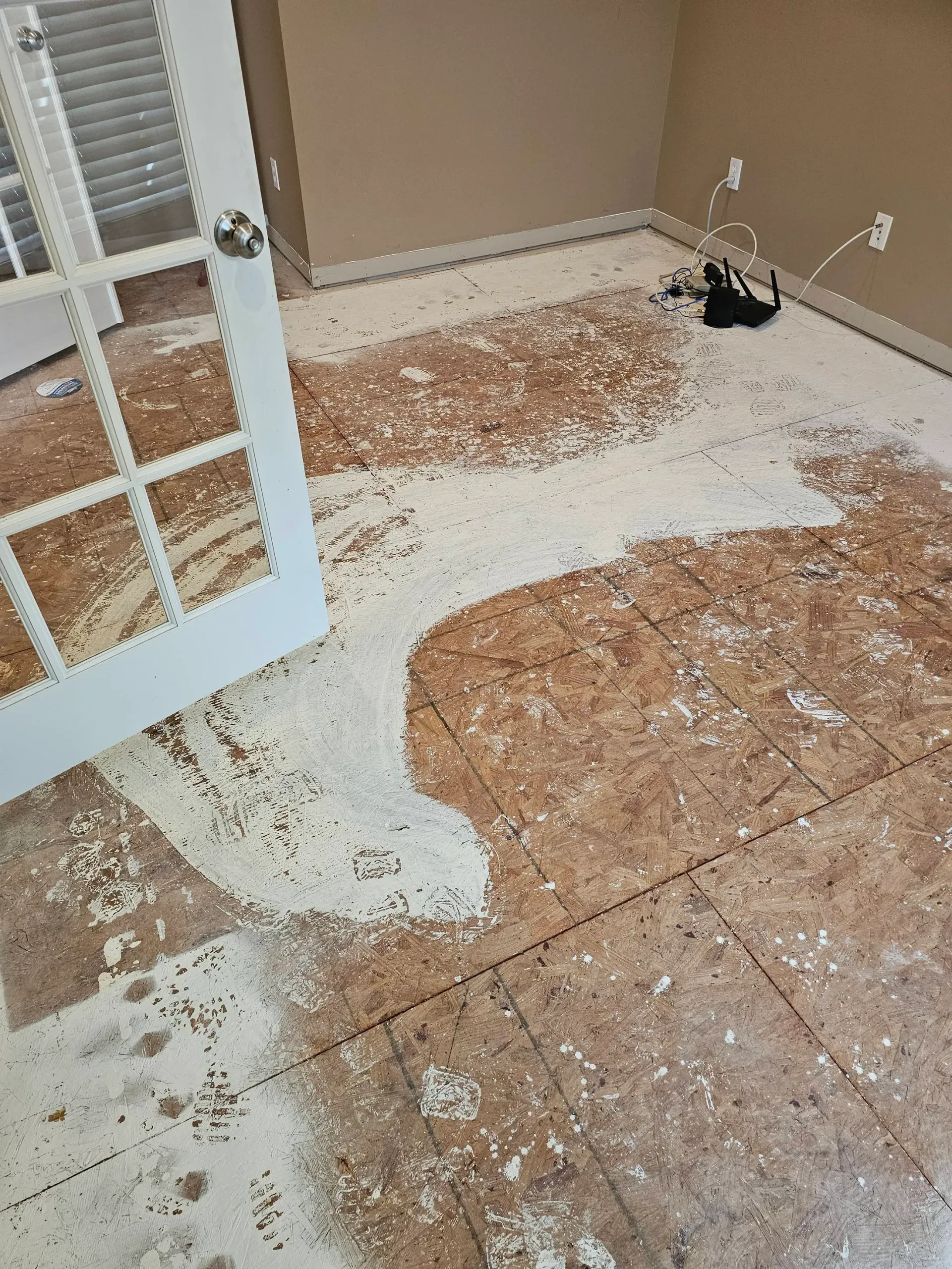 White spilled substance covers a floor with damaged brown flooring and a partially open white door.