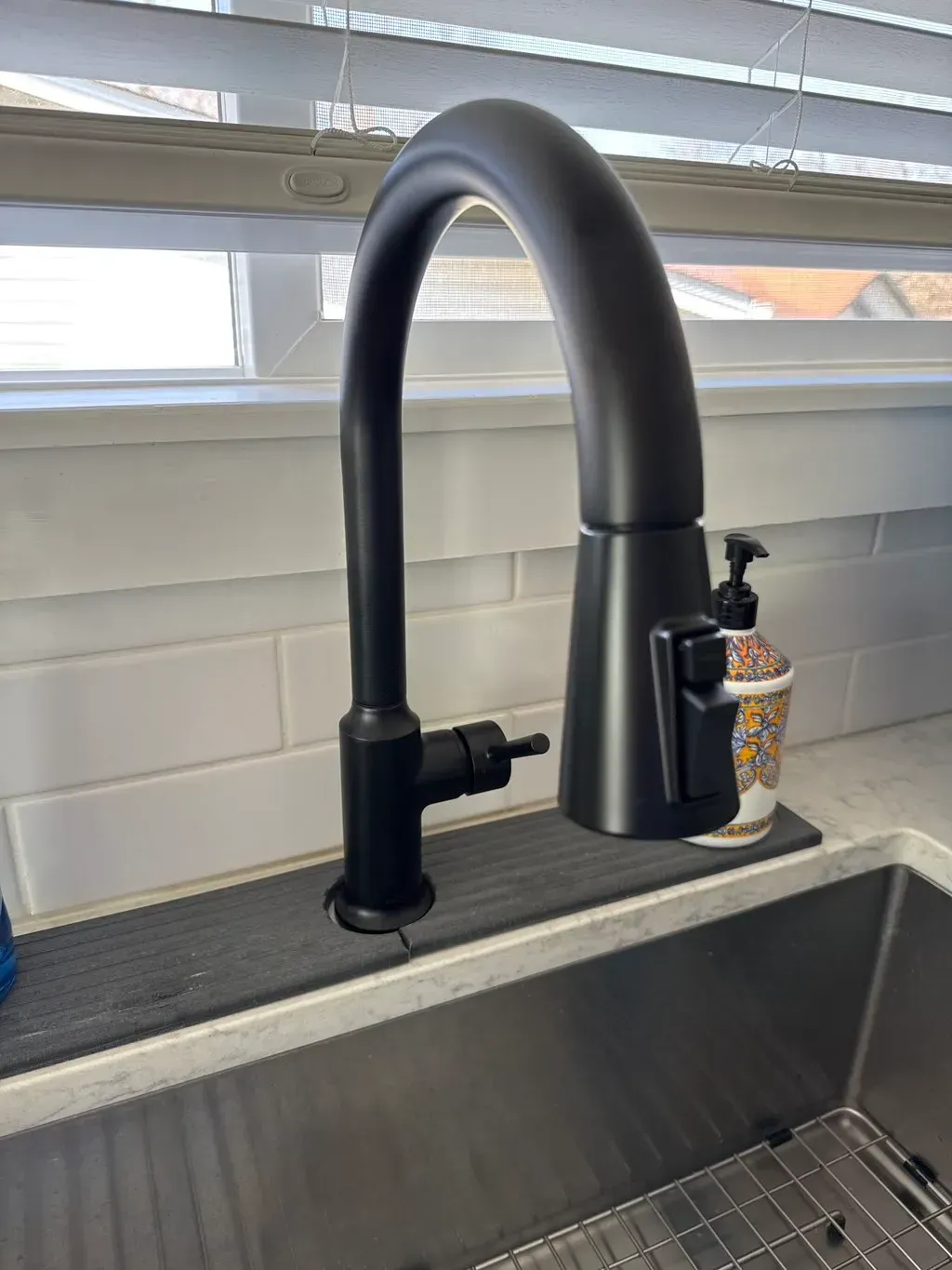 Black kitchen faucet with a pull-down sprayer and built-in soap dispenser over a stainless steel sink.