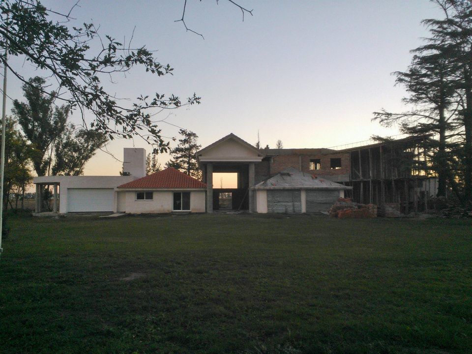 Gran casa con jardín delantero al atardecer, enmarcada por árboles y un cielo vespertino pálido.