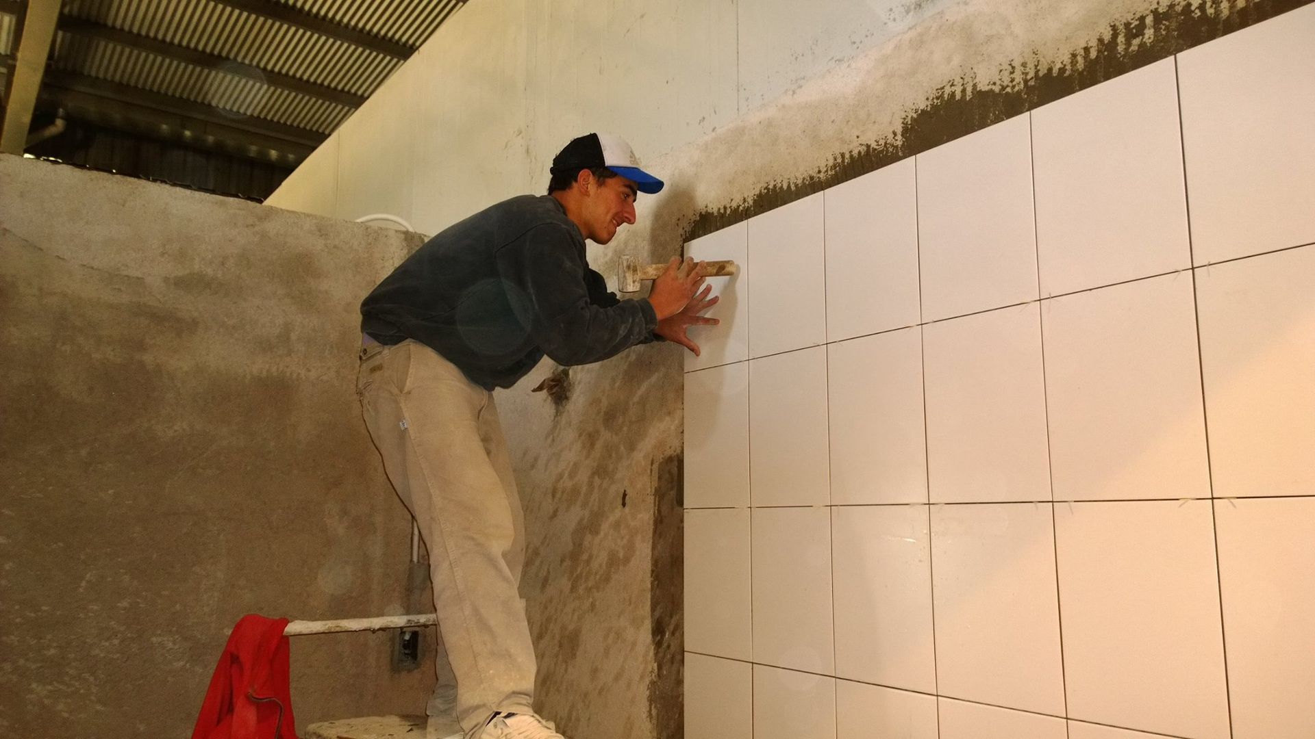 Trabajador instalando azulejos blancos en una pared en una zona de construcción.