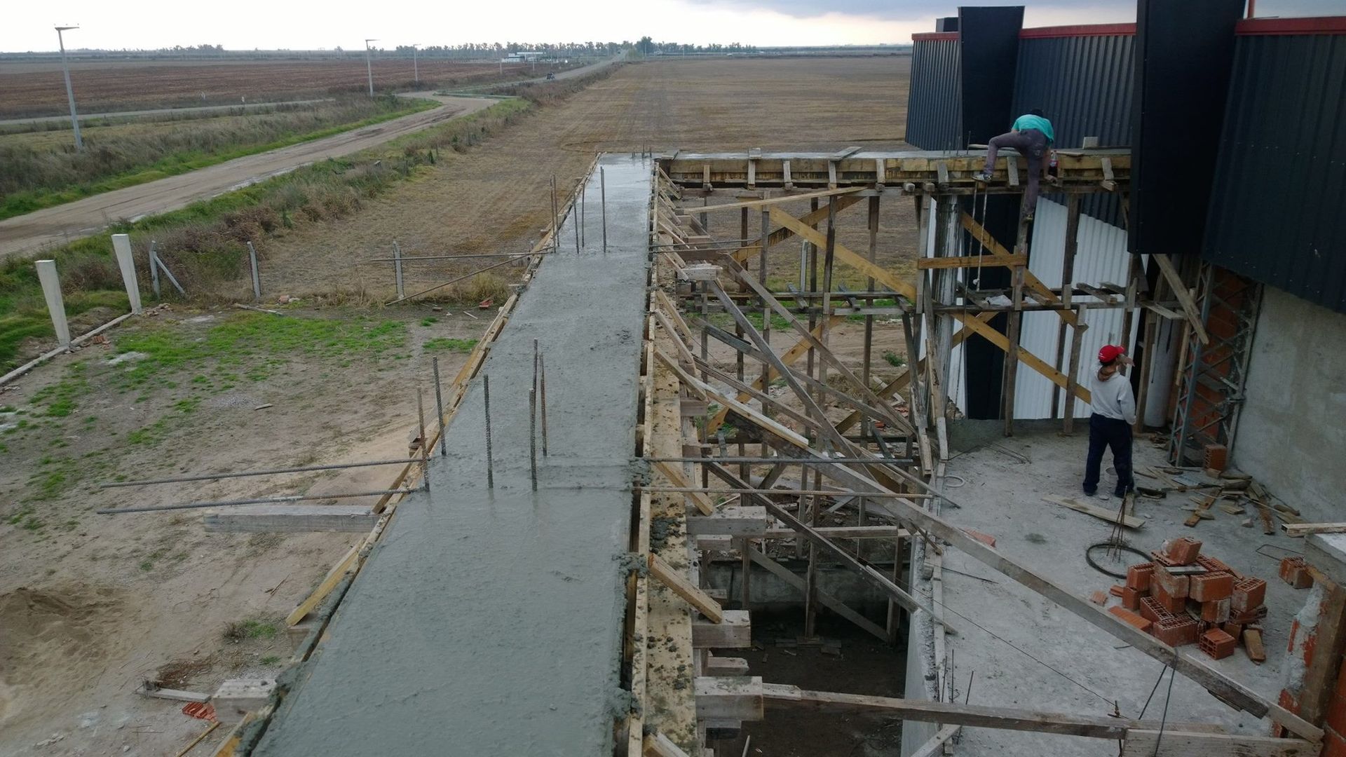 Se está vertiendo hormigón para los cimientos en una obra de construcción junto a un edificio con andamios y un terreno fangoso.