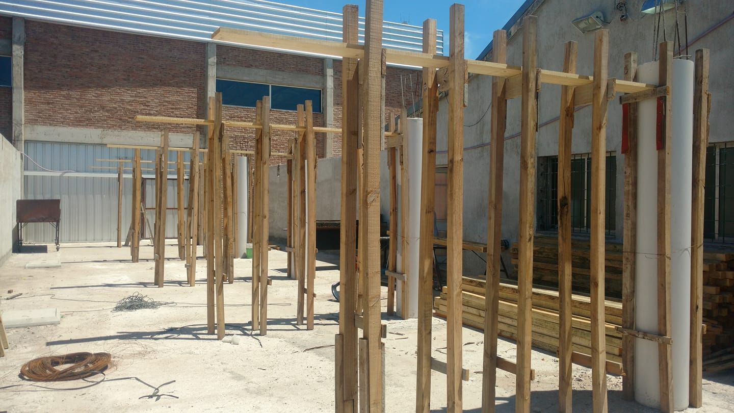 Postes de madera que enmarcan un edificio en construcción en un patio soleado.