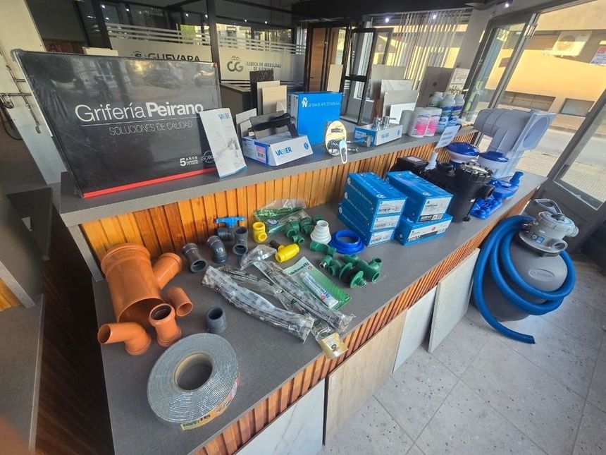 Materiales de construcción expuestos en un mostrador dentro de una tienda, incluyendo tuberías, accesorios, cinta adhesiva y herramientas.