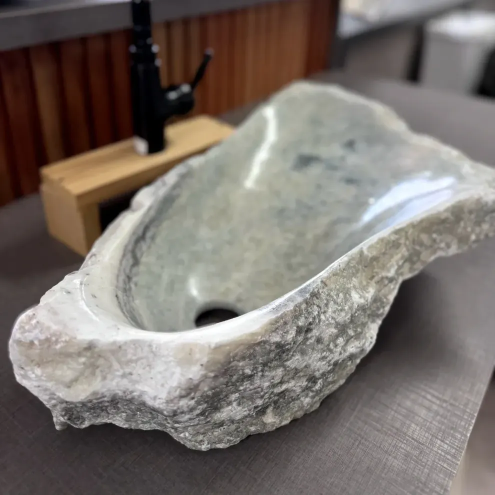 Lavabo de piedra con borde exterior rugoso sobre la encimera del baño, junto a un grifo.