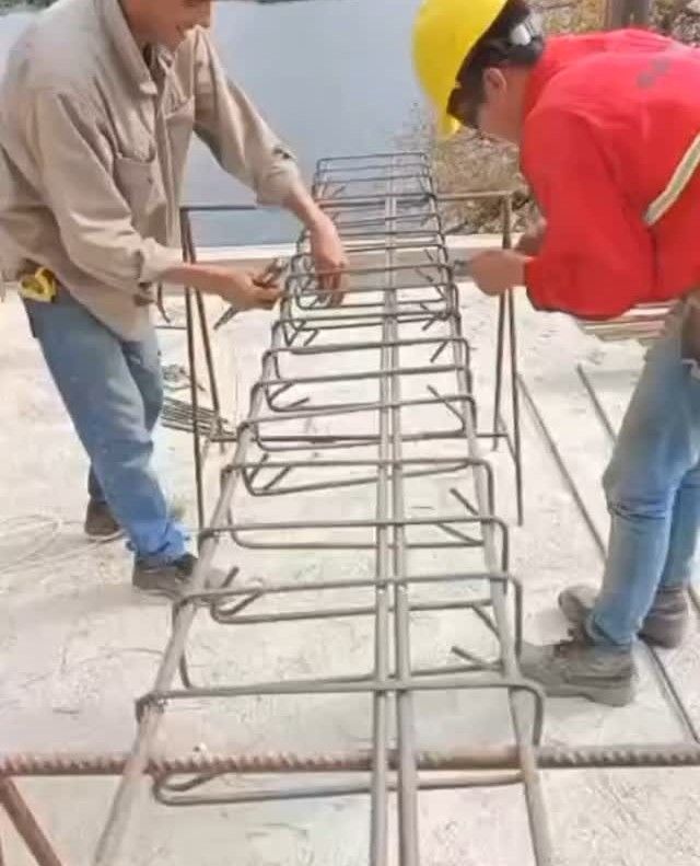 Dos trabajadores colocando barras de refuerzo sobre una losa de hormigón en una obra de construcción.