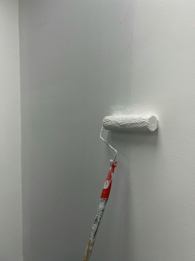Rodillo de pintura aplicando pintura blanca sobre una pared gris.