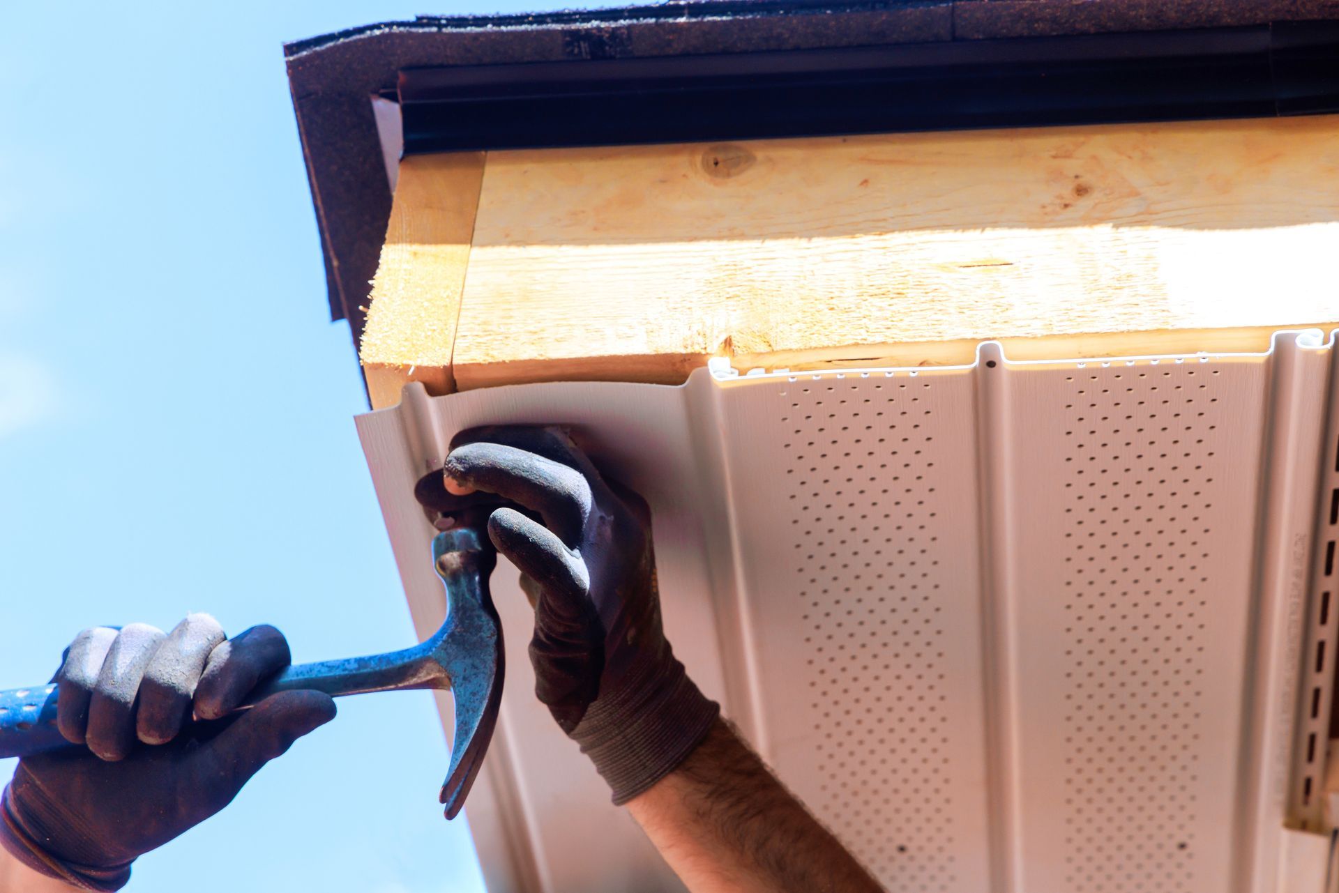 A worker installs roof flashing while standing on a ladder in a residential area.