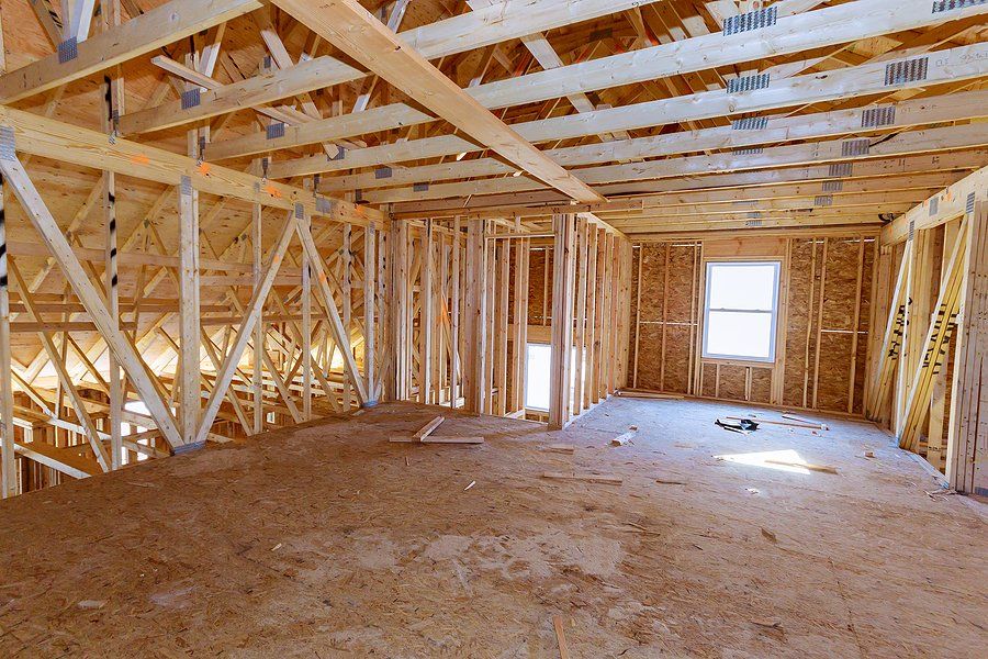 Unfinished wooden room framing with exposed beams, studs, and a single window letting in daylight