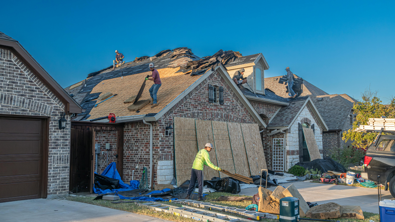 Workers replacing a damaged roof on a brick home.