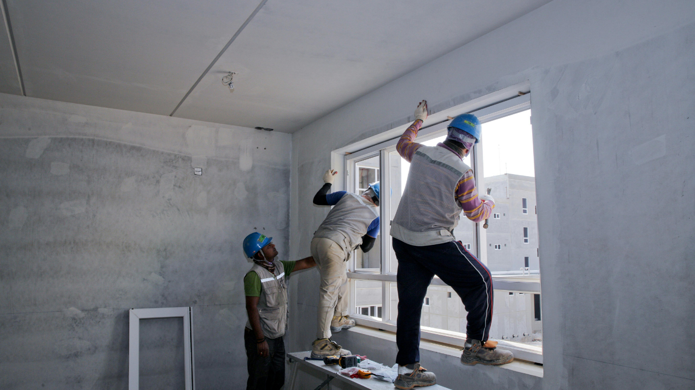 Construction workers installing a window in a building. Workers are wearing helmets.