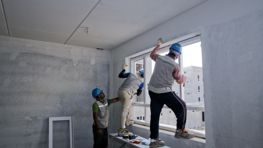 Construction workers installing a window in a building. Workers are wearing helmets.