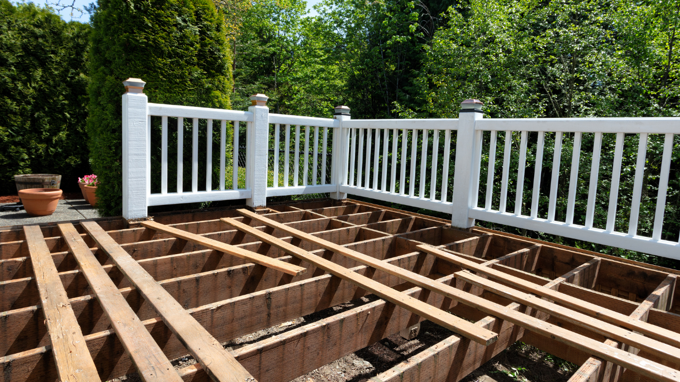 Deck under construction with white railing and surrounding greenery.