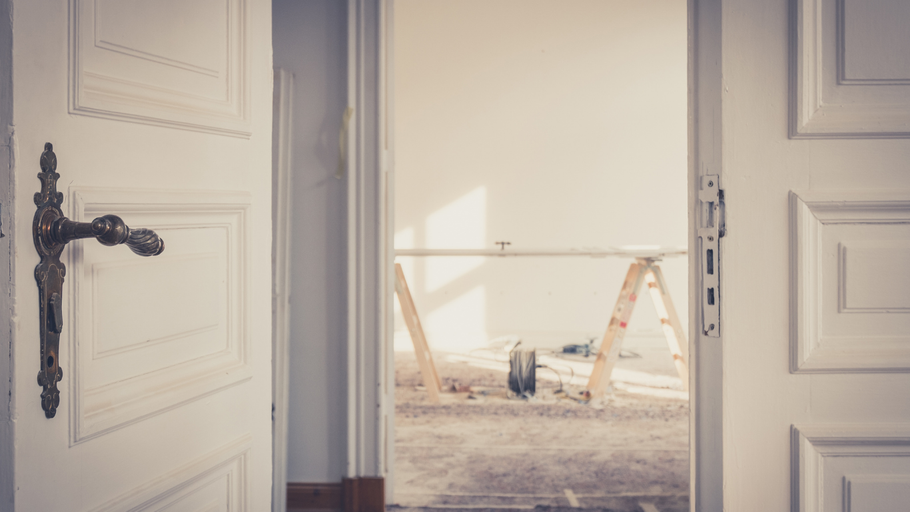 Open white door reveals a room under renovation; ladder, dust, and tools are visible.