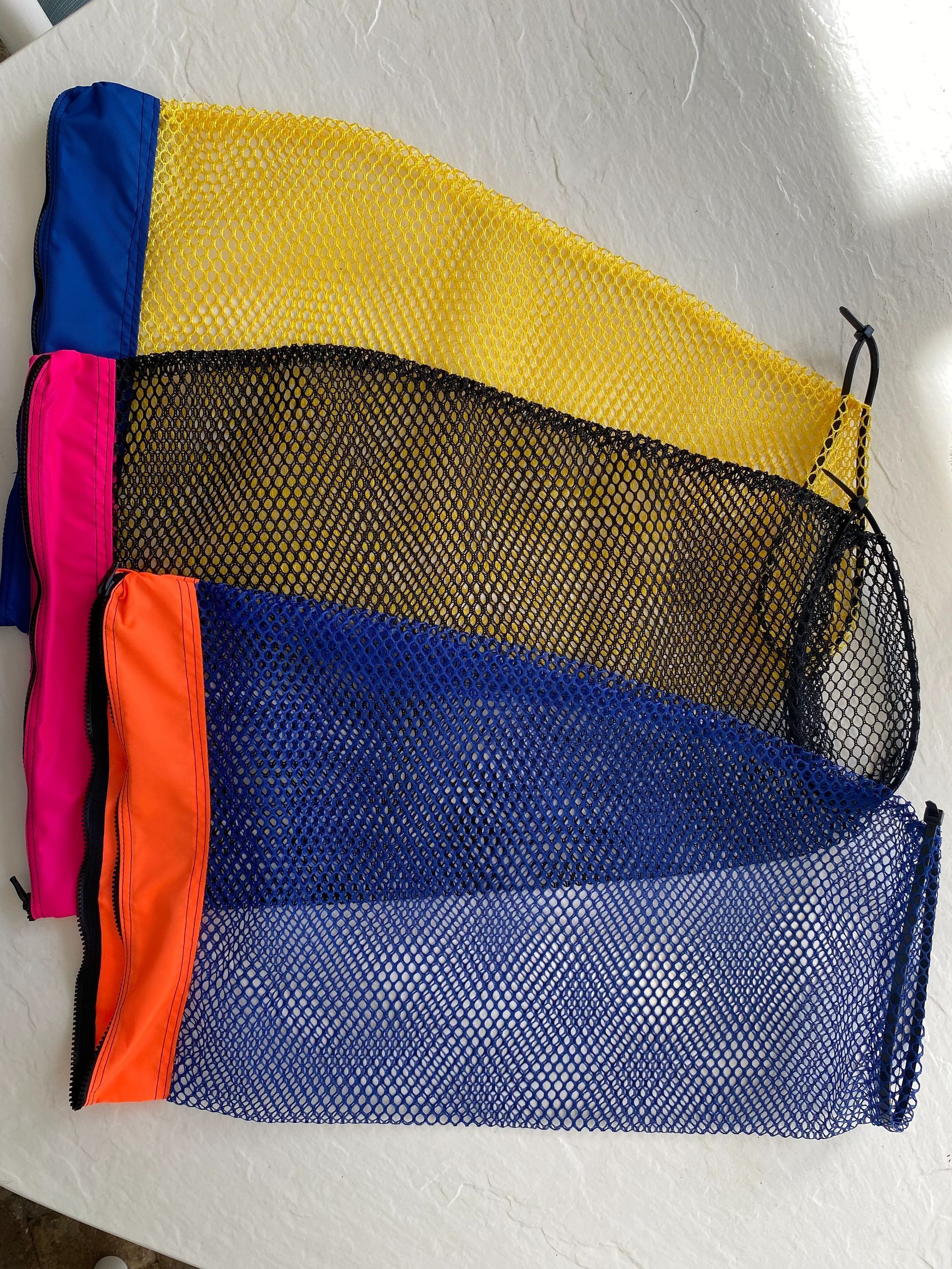 Four mesh bags with colored tops: blue, yellow, black, and dark blue, laying on a white surface.