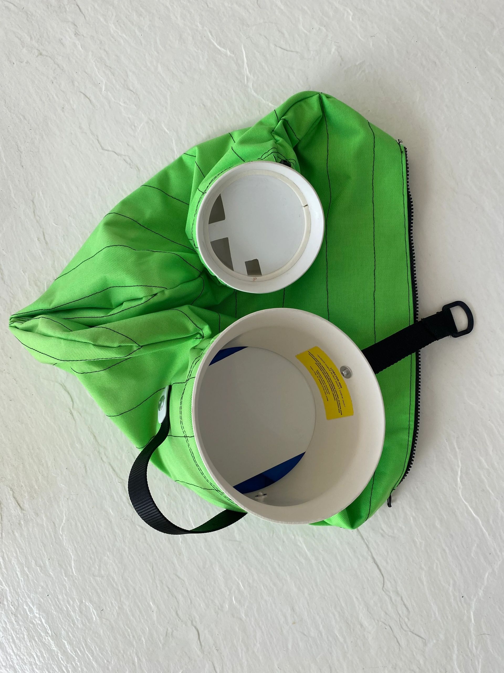 Lime green bag with a white cooking pot and lid on a light-colored surface. Black handle.