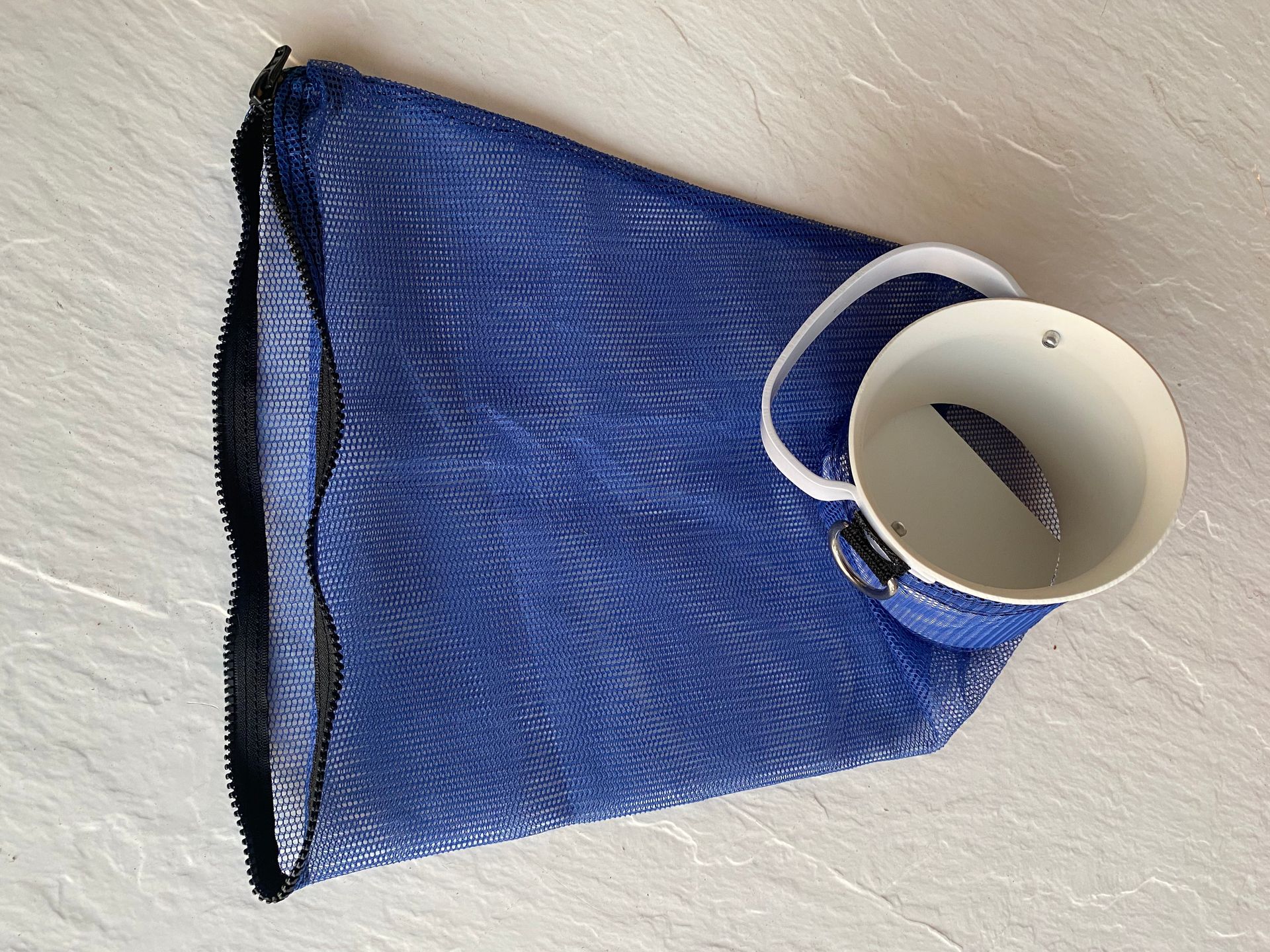 Blue mesh laundry bag with a white porcelain cup inside, on a light gray surface.