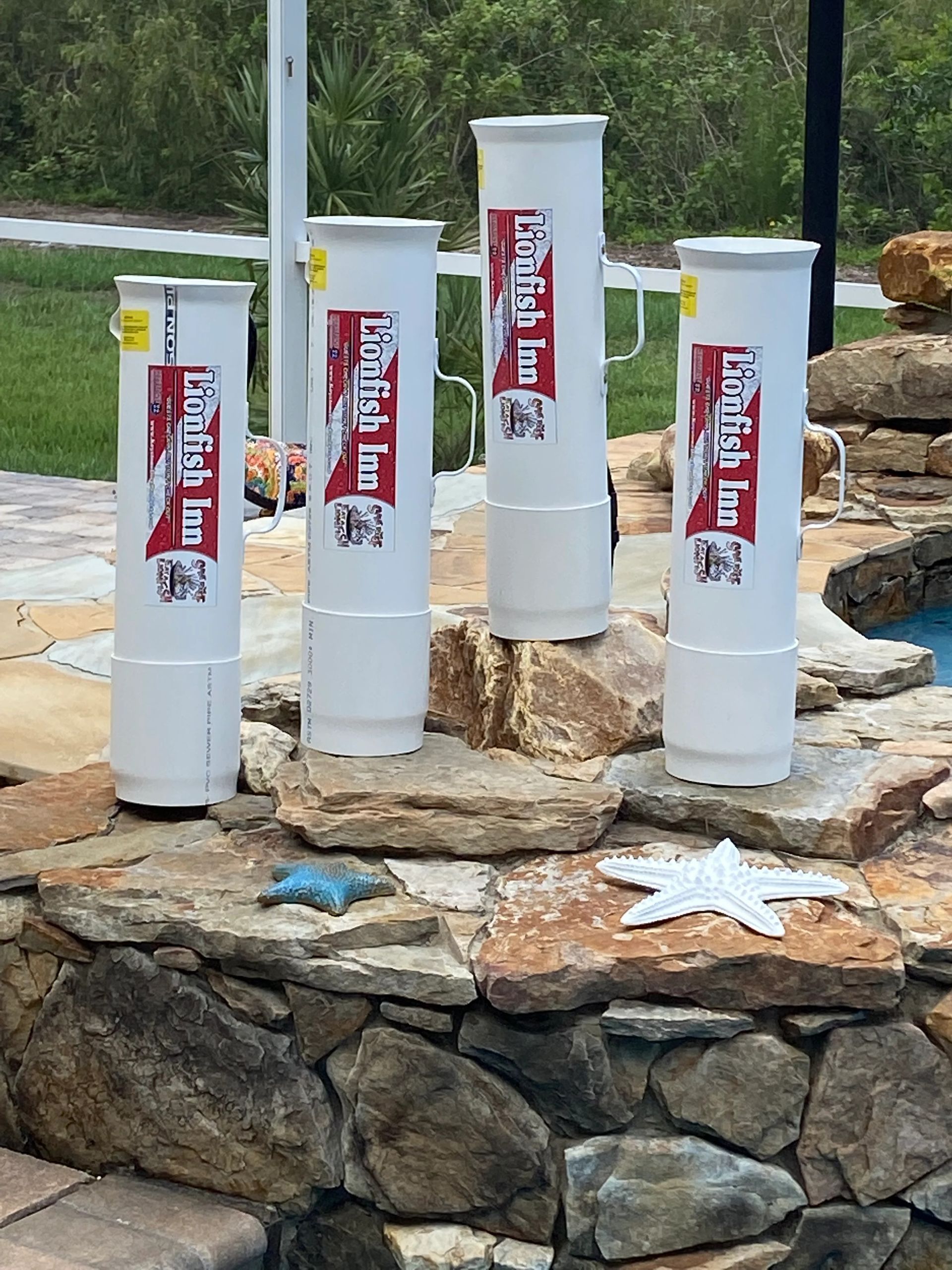 Four white cylinders with red labels on a stone wall by a pool.