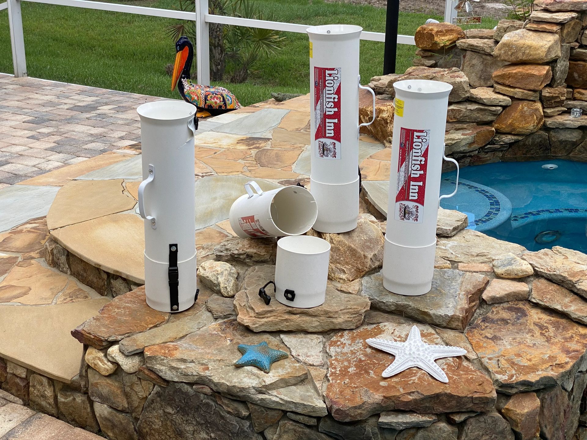 Four white cylinders with red labels on a stone wall by a pool.