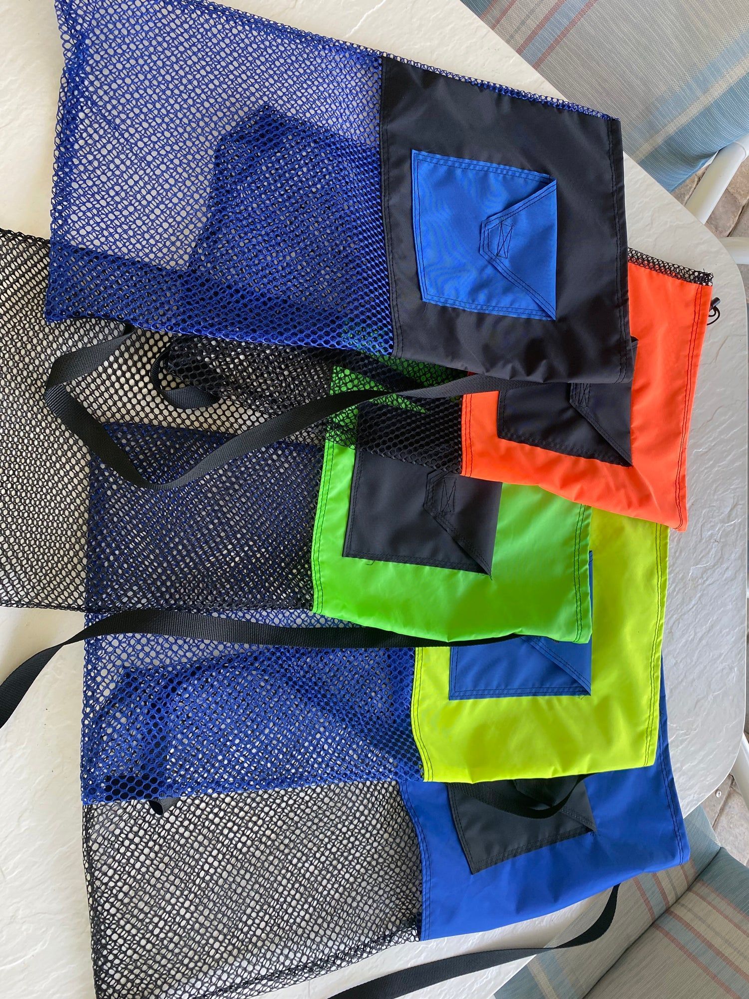 Mesh bag with blue, black, green, and orange fabric pockets, and black straps, on a white table.
