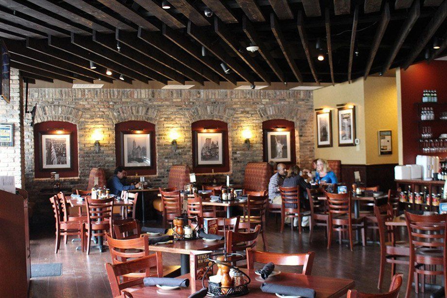Interior of a restaurant with exposed brick walls, dark wood tables and chairs, and customers seated at tables.