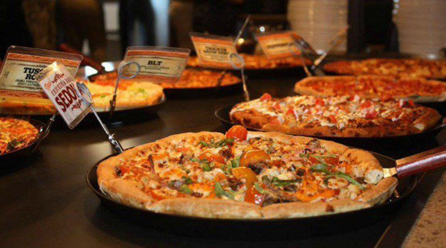 Pizzas in various flavors on display at a restaurant. Close-up of a pizza with toppings and a sign reading