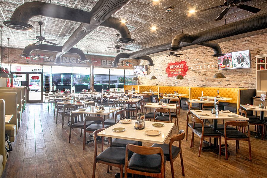 Interior of a restaurant with tables, chairs, booths, exposed brick walls, and ventilation ducts. 