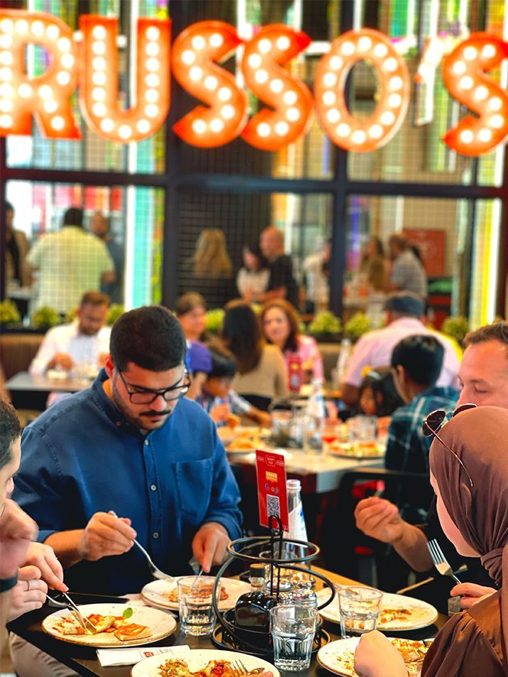 People dining inside Russo's restaurant. A man in a blue shirt and glasses eats, surrounded by other diners at tables.