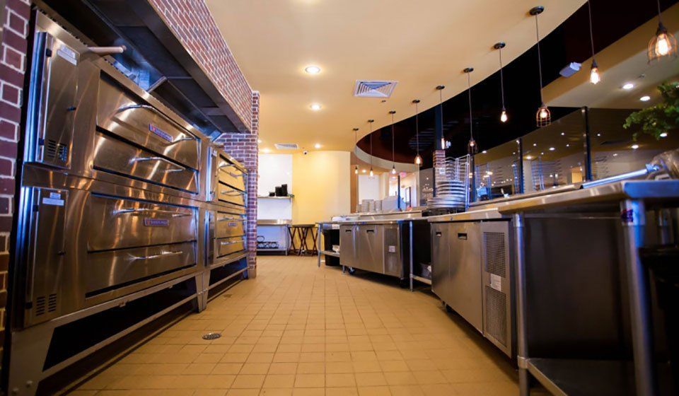 Commercial kitchen with stainless steel appliances and ovens along one wall, a curved counter, and overhead lighting.