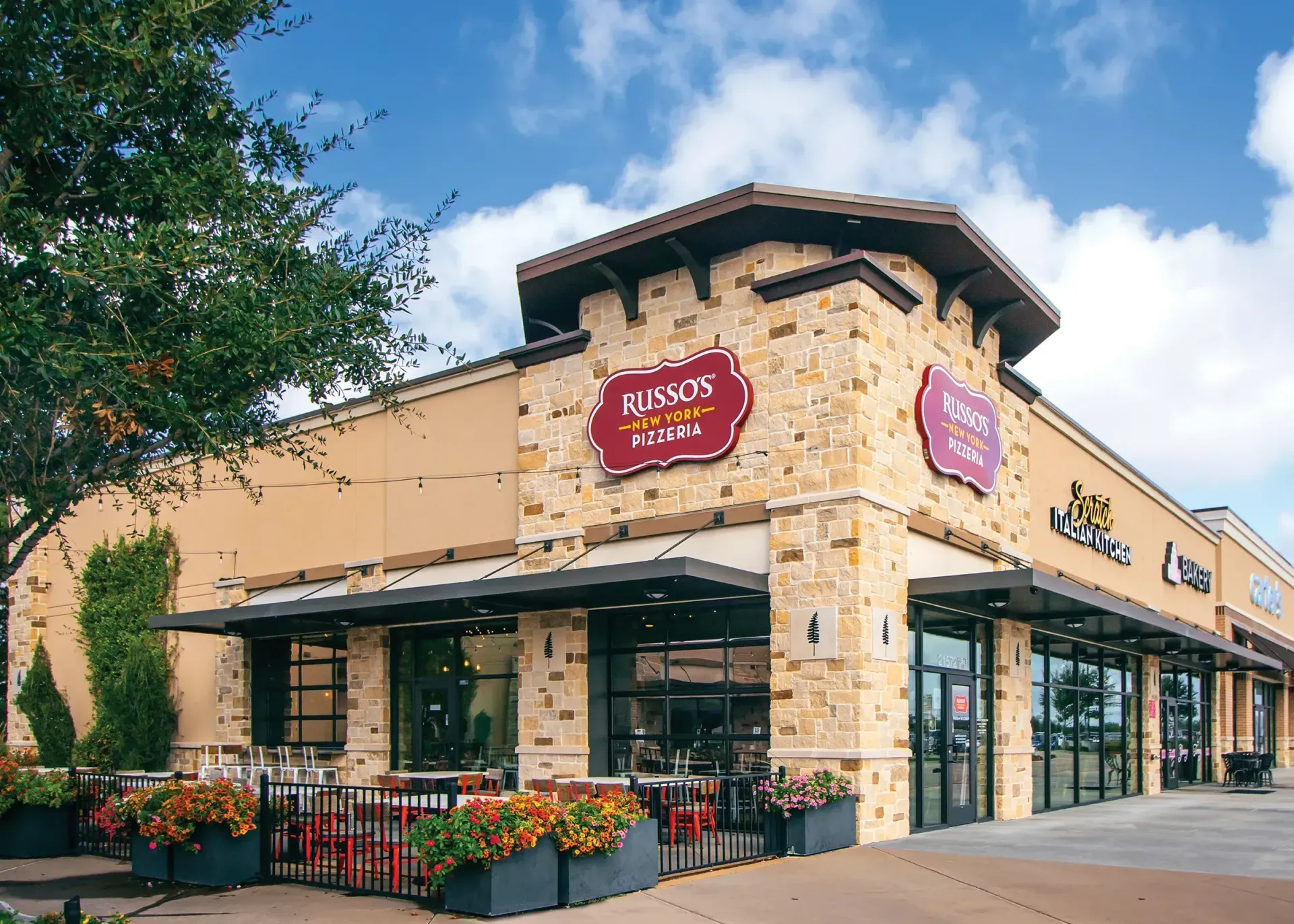 Exterior of a restaurant, Russo's Italian Kitchen, with stone facade, awnings, and outdoor seating under a blue sky.
