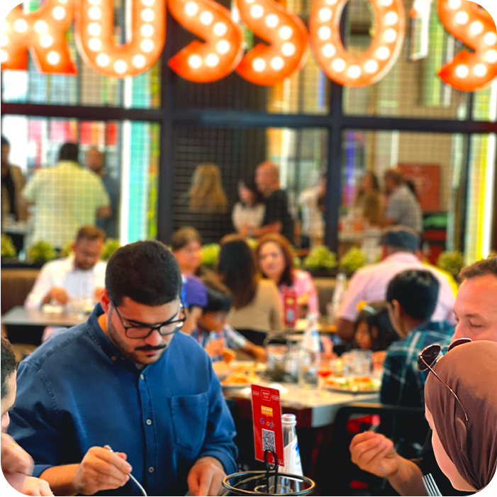 People dining inside Russo's restaurant. A man in a blue shirt and glasses eats, surrounded by other diners at tables.